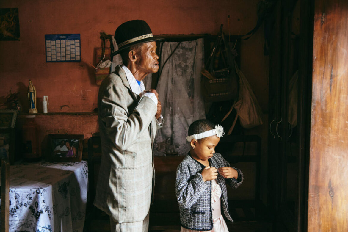 Zu sehen sind zwei Personen, ein kleines Mädchen und ein älterer Mann, die sich vor dem Spiegel fertig machen. Beide zupfen an ihrer Kleidung..  ©World Press Photo