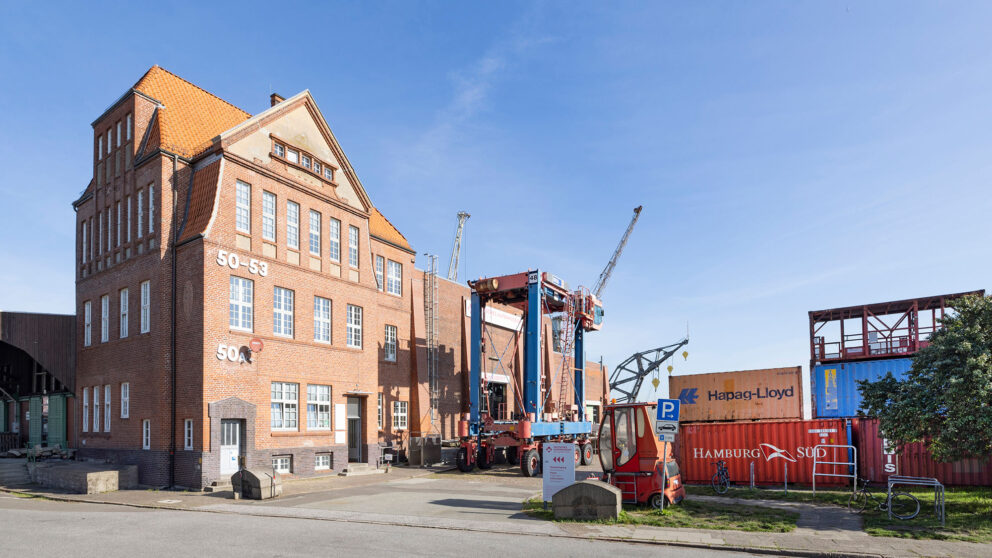 Kopfbau des Schuppens 50A im Hansahafen mit Van Carrier und Containern auf dem Vorplatz